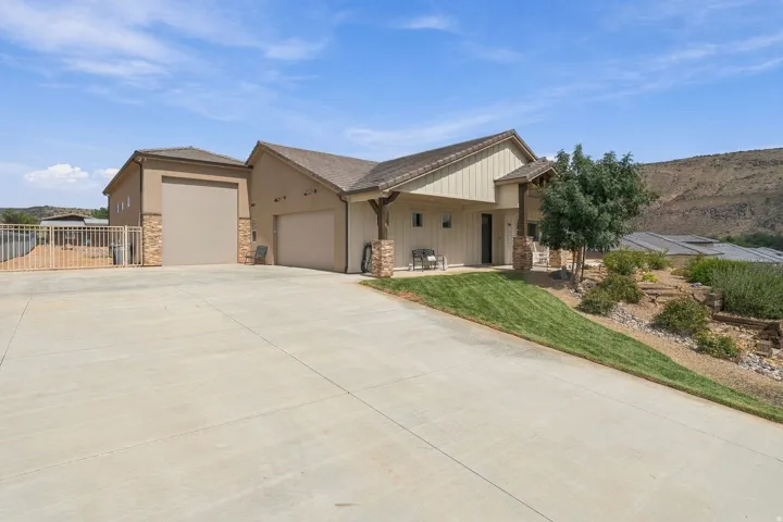 Stucco exterior with stone accents, a covered entry, an attached two-car garage, an additional garage bay, and a sloped lawn with desert landscaping