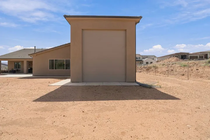 Detached utility building with a roll-up door, adjacent to a stucco-finished residence