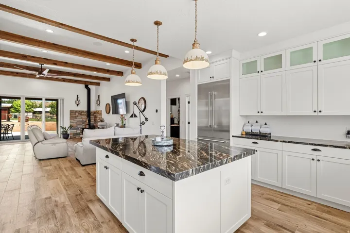 Open-concept living space with exposed wood beams, wood-finish flooring, and a stone-clad fireplace
