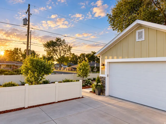 Board and batten siding, attached garage, concrete driveway, stone veneer accents, and white privacy fencing