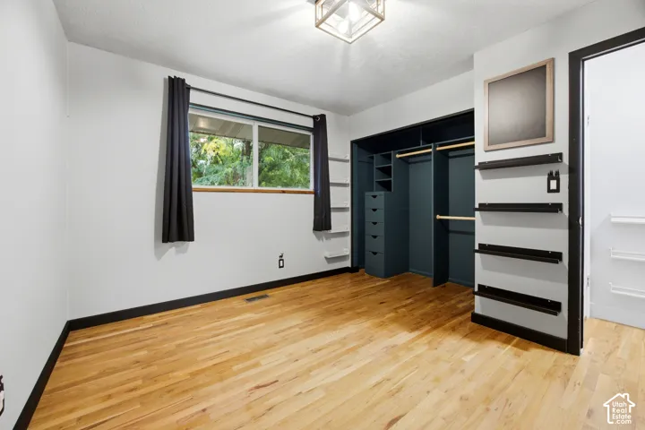 Wood-finish flooring, built-in closet system with drawers and shelving, recessed lighting, and a large window