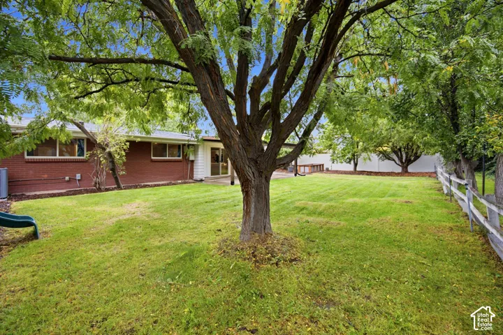 Expansive green lawn, mature trees, white picket fence, brick exterior, and a sliding glass door