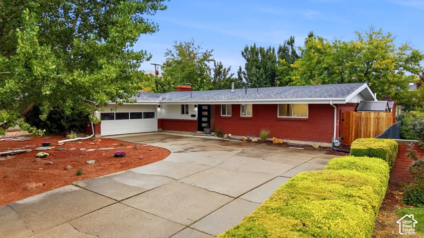 Red brick exterior, attached garage, concrete driveway, mature landscaping, and privacy fencing