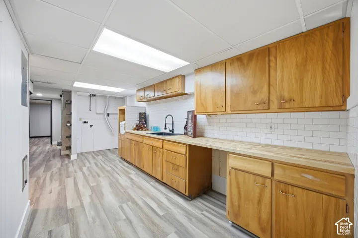 Wood-finish flooring, white subway tile backsplash, wood cabinetry, and a black sink with a matte black faucet