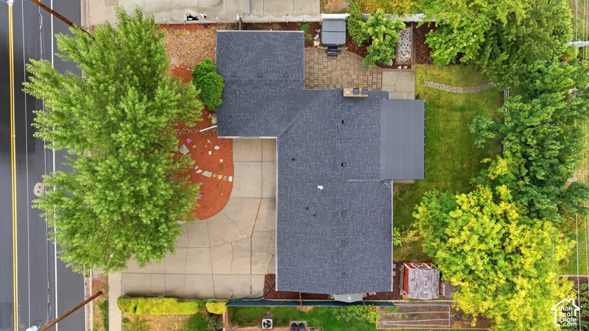 Asphalt shingle roofing, paved driveway, paver patio, established landscaping, and a grassy lawn area