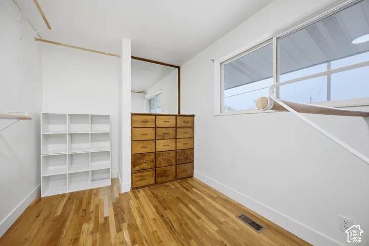 Bright, versatile room featuring hardwood flooring, abundant natural light from large windows, and ample storage with built-in white shelving and vintage wooden cabinetry
