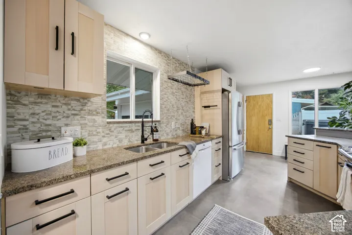 Light-toned cabinetry with matte black hardware, granite-style countertops, stainless steel appliances, a double basin sink with a black fixture, and a skylight