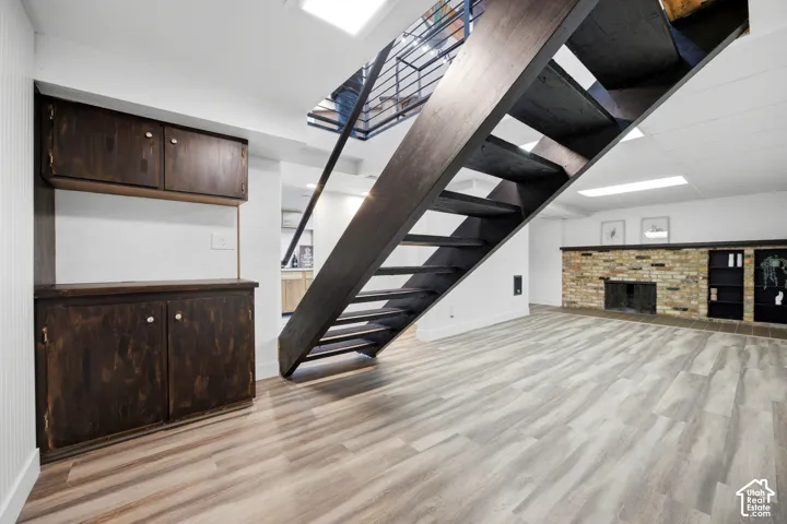 Wood-finish flooring, open tread staircase, built-in cabinetry, brick fireplace, and recessed lighting