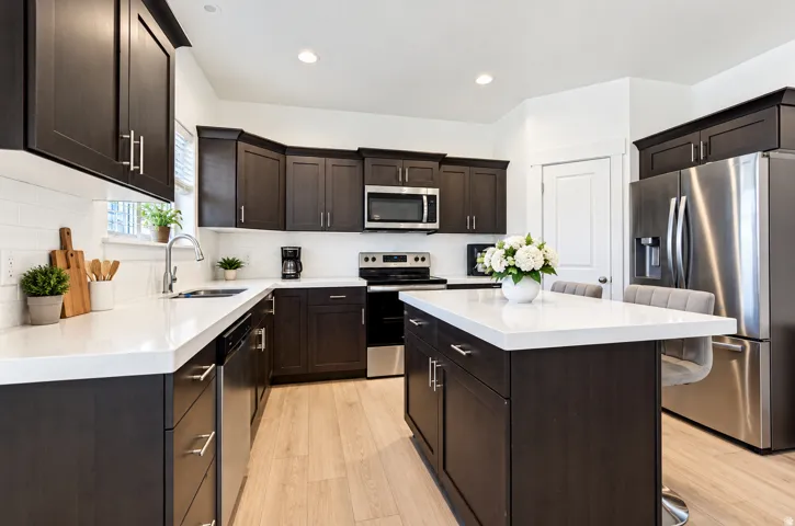 Kitchen featuring dark wood-finish cabinetry, stainless steel appliances, a white tile backsplash, a center island with a white countertop, and wood-finish flooring