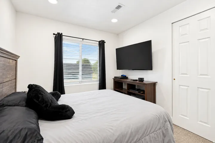 Recessed lighting, wood-finish headboard, window with blinds, wall-mounted television, and a built-in media console