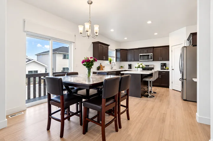 Open-concept kitchen and dining area featuring light wood-finish flooring, dark wood cabinetry, stainless steel appliances, and a kitchen island with seating