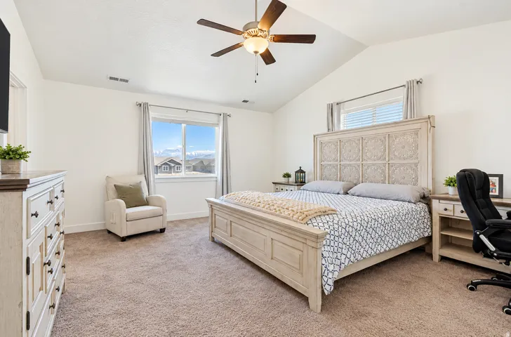 Vaulted ceiling with a ceiling fan, carpet flooring, and window with a mountain backdrop