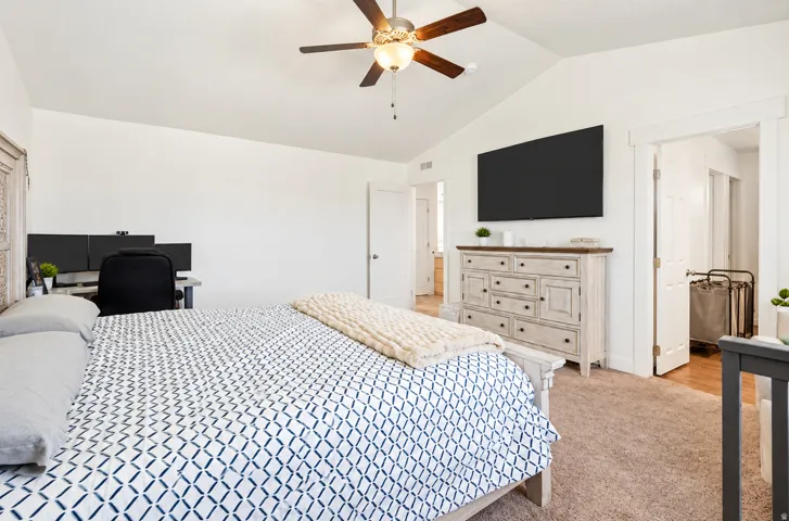Vaulted ceiling with a ceiling fan, white paneled doors, wall-mounted television, and wood-finish flooring