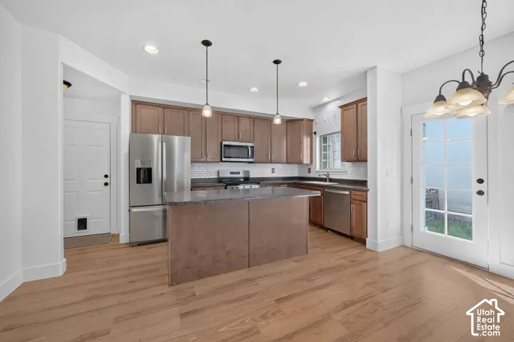 Kitchen featuring wood-finish cabinetry, stainless steel appliances, a center island with counter seating, pendant lighting, and a white subway tile backsplash