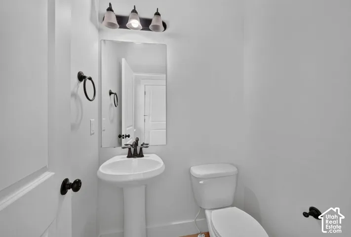 Pedestal sink with dark bronze fixtures, rectangular mirror, and three-light vanity bar