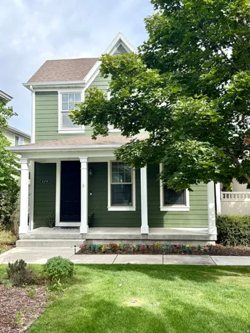 Two-story residence with green siding, a covered front porch with white columns, and a landscaped front yard
