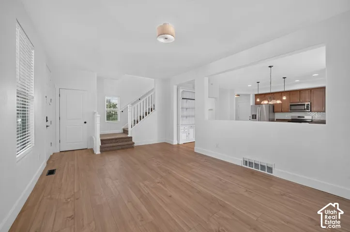 Open-concept living space featuring wood-finish flooring, white walls, and a staircase with carpeted treads
