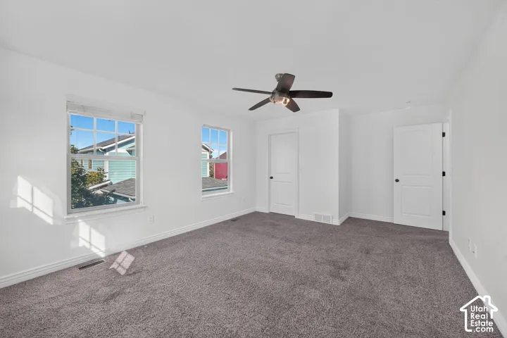 Spacious room featuring neutral carpeting, two windows, two white panel doors, and a ceiling fan