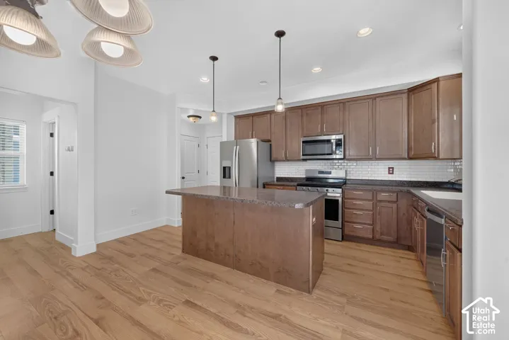 Open-concept kitchen with wood-finish flooring, stainless steel appliances, a center island with countertop, and white subway tile backsplash