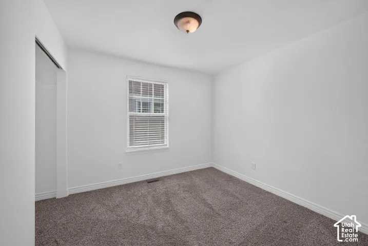 Plush carpet flooring, white painted walls, a double-paned window, and a built-in closet with sliding doors