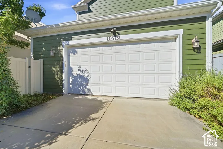 Attached garage with a white panel door, featuring green siding and an overhead exterior light fixture