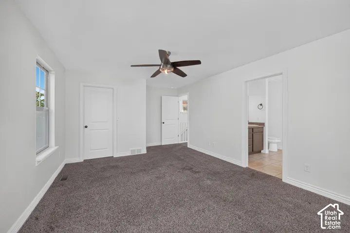 White walls, gray carpeting, and a ceiling fan with light fixture