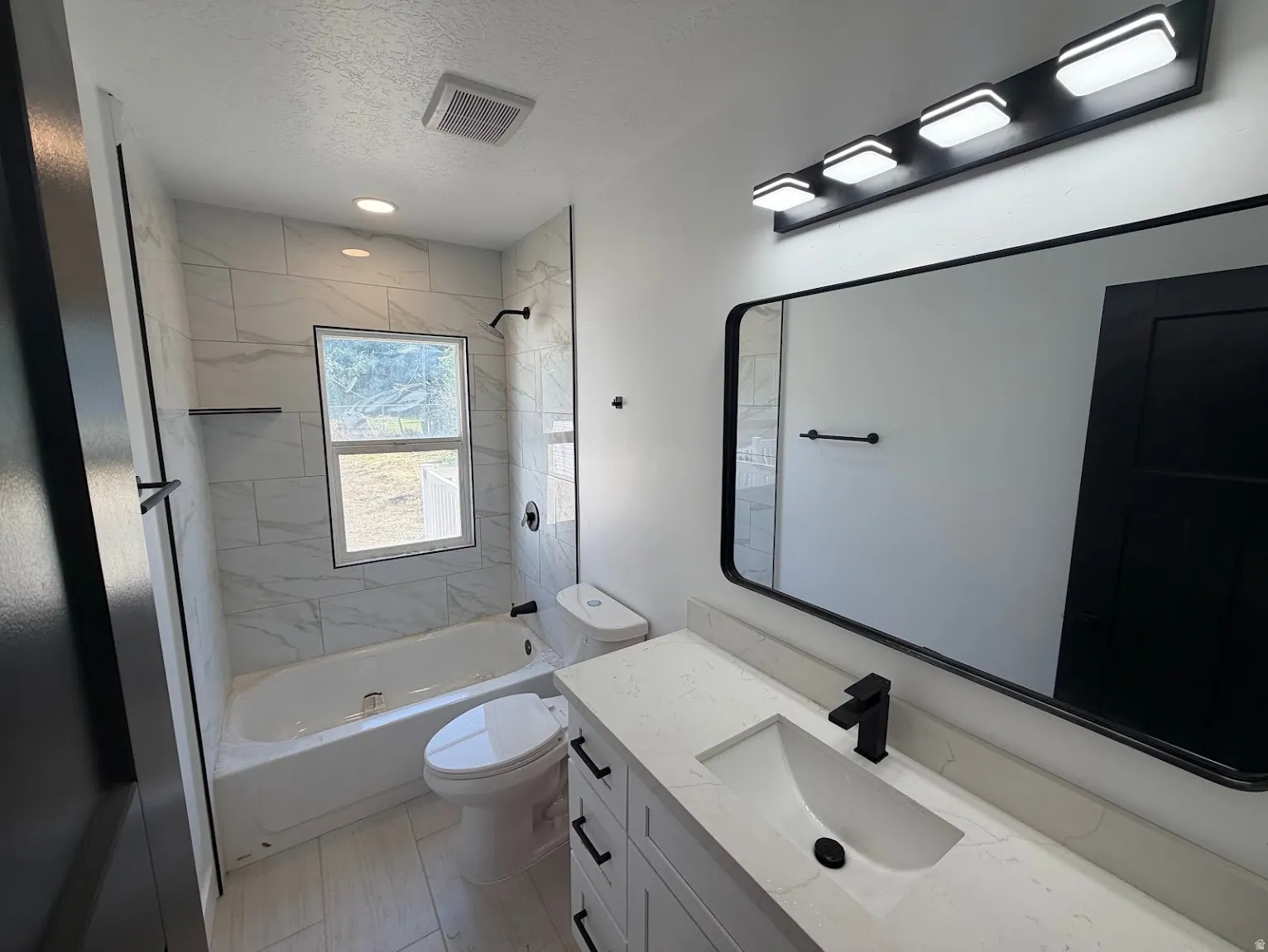 Bathroom featuring a single vanity with an integrated sink, black fixtures, a rectangular mirror, and a tiled tub shower