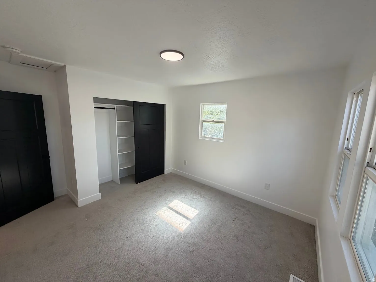 Neutral-toned carpeting with white walls, black sliding closet doors, and built-in closet shelving