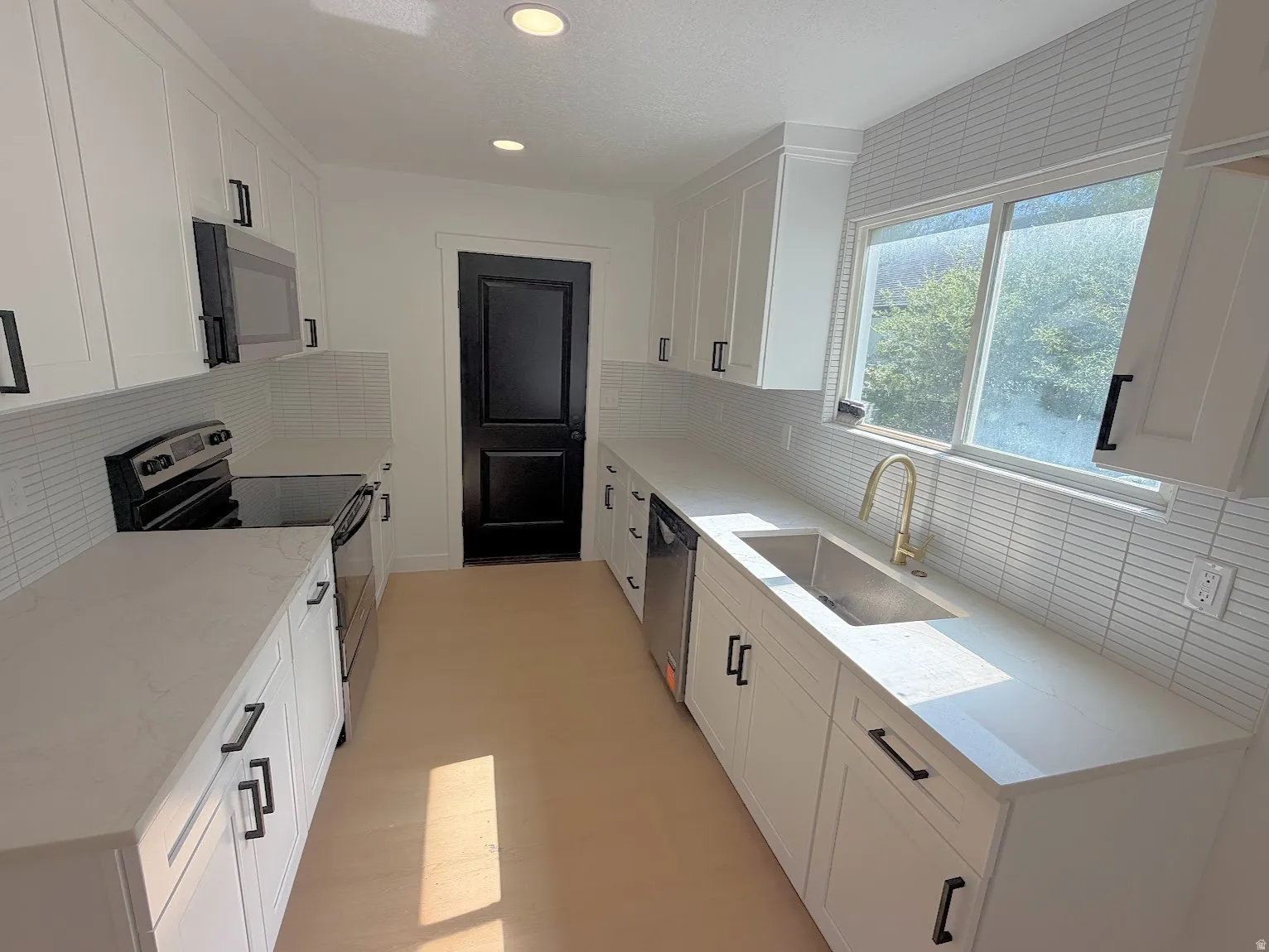 White shaker cabinetry, light-toned countertops, white horizontal tile backsplash, stainless steel appliances, and wood-finish flooring