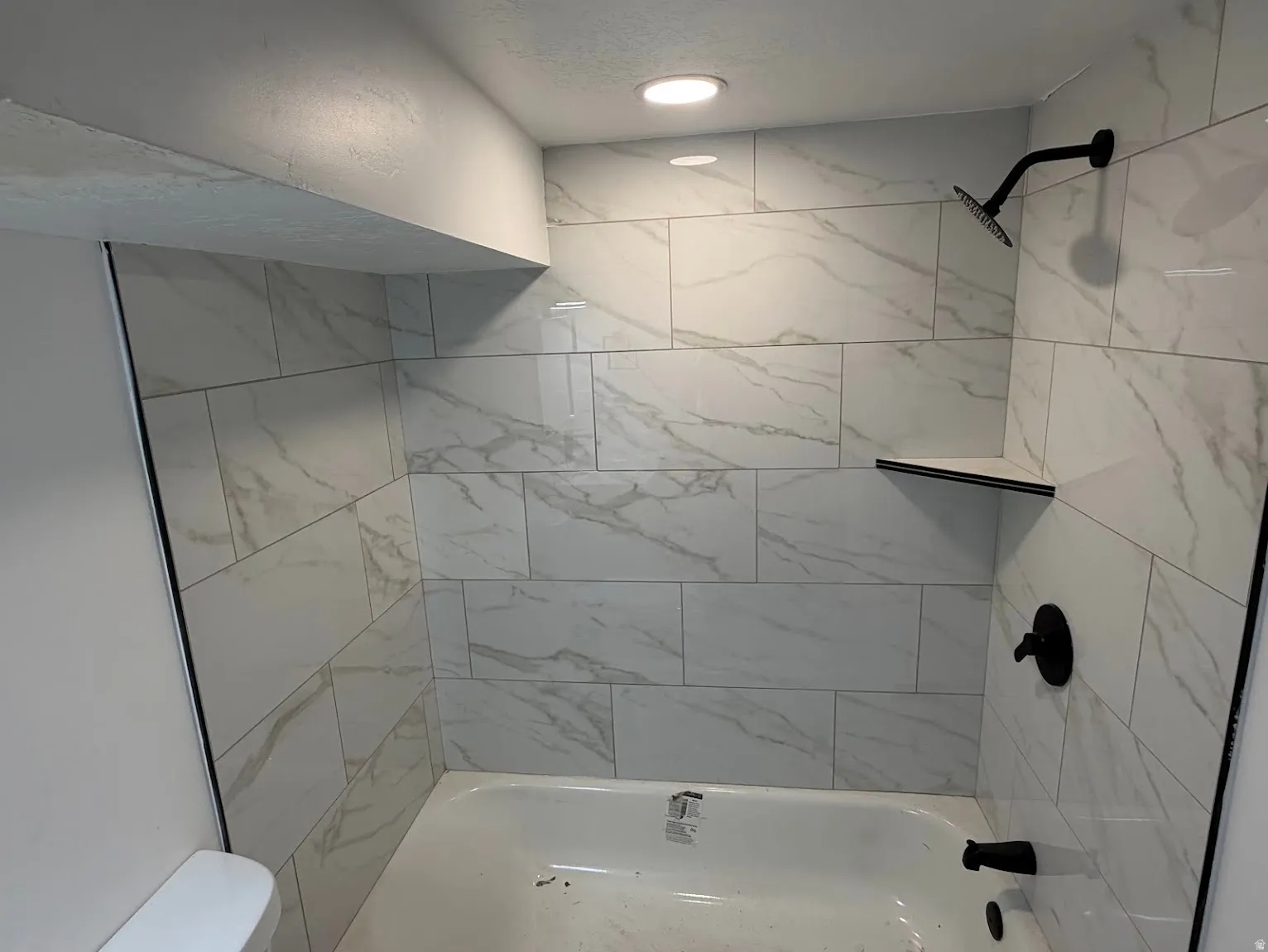 Tub with white subway tile surround, recessed lighting, and matte black fixtures