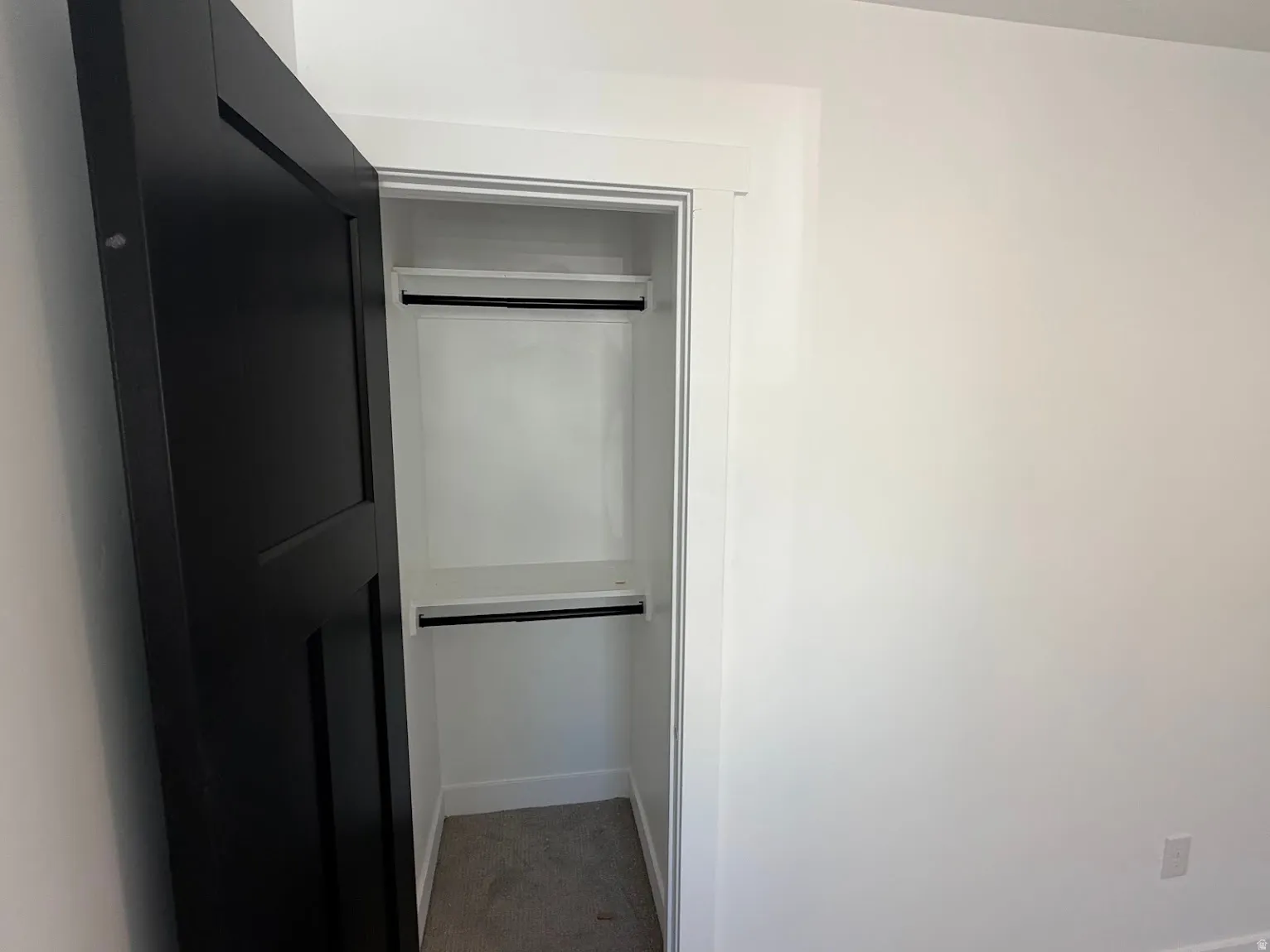 Recessed closet featuring a black paneled door, white trim, and a built-in shelf with hanging rods