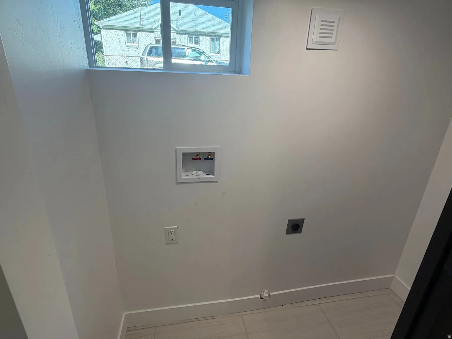 White walls with a single window, a washer hookup, and tiled flooring