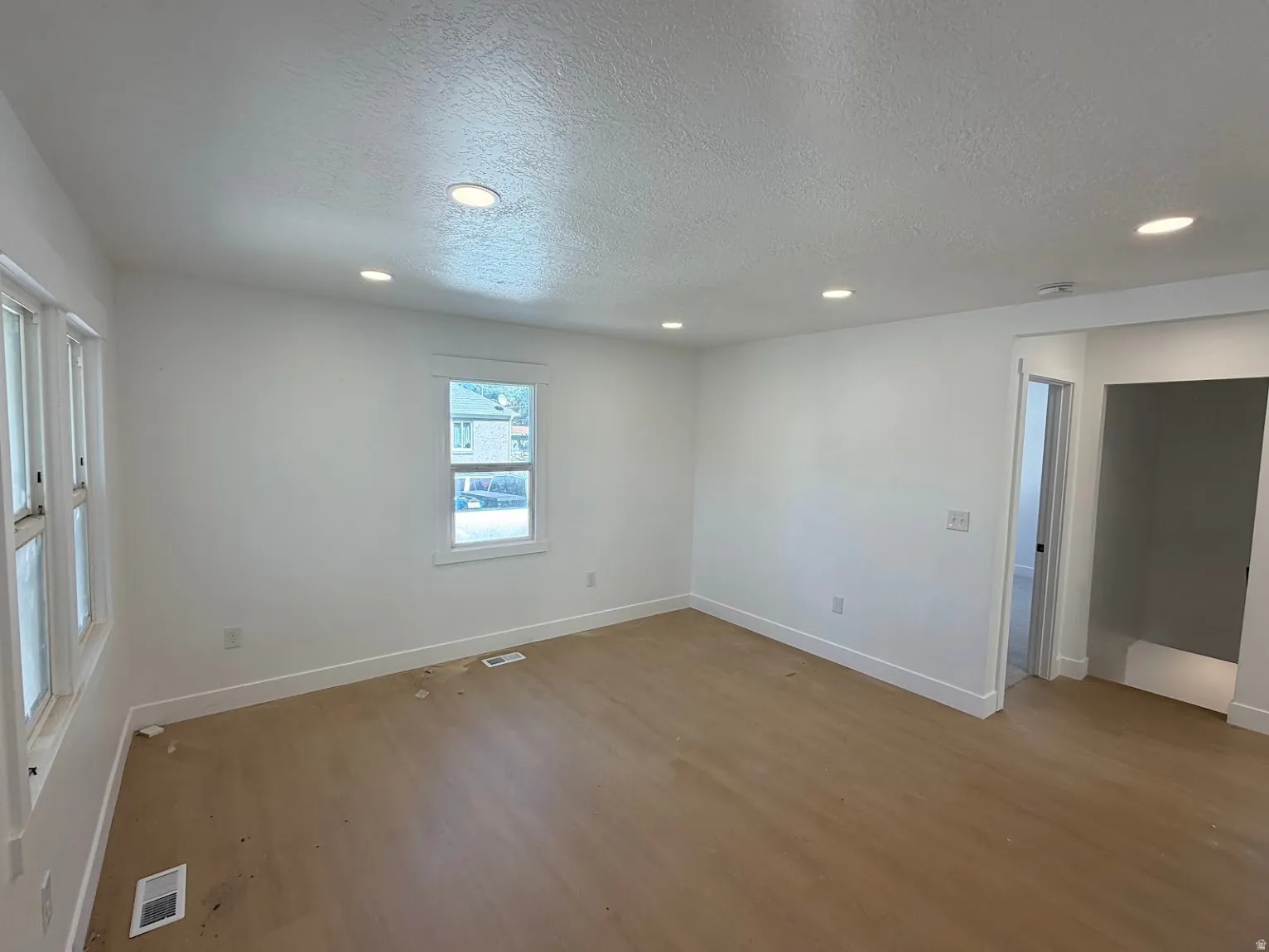 Recessed lighting illuminates the room with wood-finish flooring and white painted walls