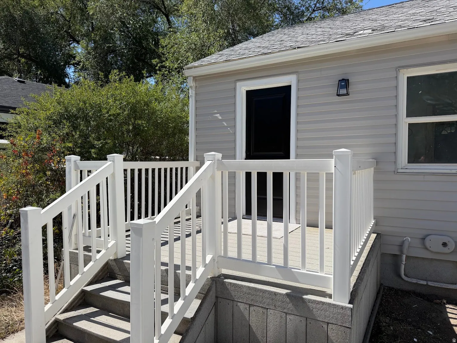 Exterior featuring light-colored siding, a dark entry door, and a white railing system with integrated stairs