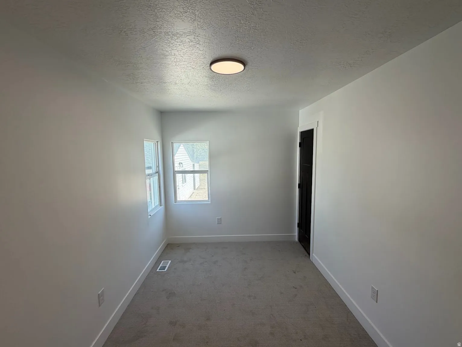 Neutral paint palette, textured ceiling, two windows, carpeted flooring, and a dark-paneled door