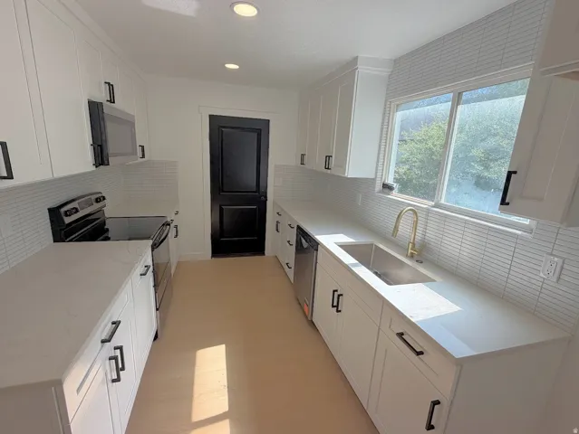 White shaker cabinetry, light-toned countertops, white horizontal tile backsplash, stainless steel appliances, and wood-finish flooring