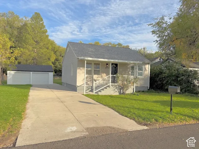 Single-story residence featuring light-colored siding, a covered front porch with metal railings, a concrete driveway, and a detached two-car garage