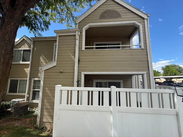 Two-story exterior with horizontal siding, featuring a private balcony and a ground-level patio enclosed by a white privacy fence