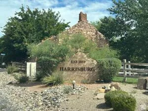 Stone monument with "Harrisburg" engraving, established 1859, surrounded by mature trees and desert landscaping at the entry of Harrisburg.