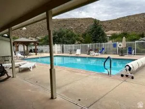 Community outdoor swimming pool with concrete decking, a white privacy fence, and a wooden gazebo