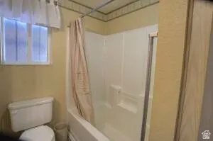Built-in bathtub with shower, white commode, and a window for natural illumination