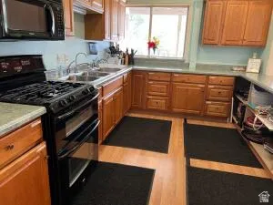 Full kitchen featuring light wood cabinetry, double basin sink, black range oven, and wood-finish flooring make a great place for events.