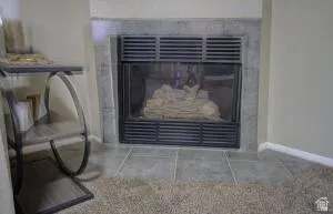 Close up of the built-in fireplace with a dark metal grate, stone surround, and tile hearth
