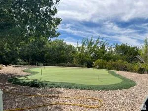 Putting green with multiple flagsticks, surrounded by decorative gravel and lush perimeter landscaping