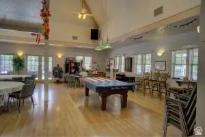 Vaulted ceiling with exposed beams, light wood-finish flooring, recessed wall sconces, ceiling fan, and multiple transom windows  around the billards Table.