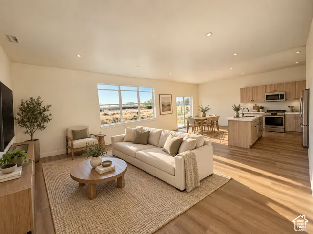 Open-concept living space featuring a cream upholstered sofa, wood-finish flooring throughout, and abundant natural light from expansive windows