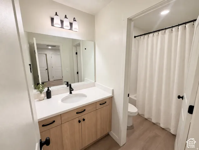 Modern bathroom featuring a wood-finish vanity with black hardware, white countertop, rectangular mirror, and a shower-tub combination