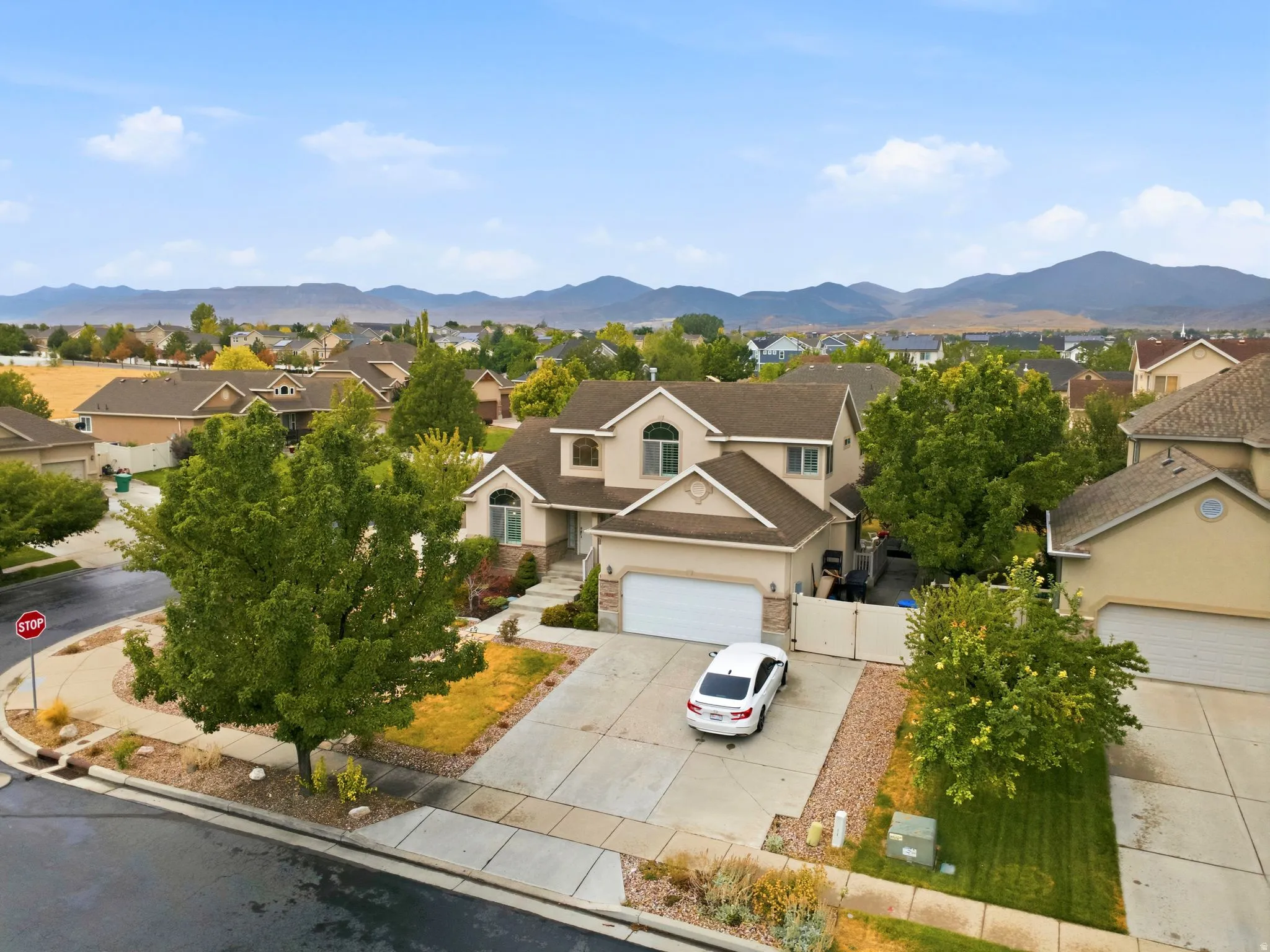 Two-story stucco exterior with arched windows, attached two-car garage, concrete driveway, and mature landscaping