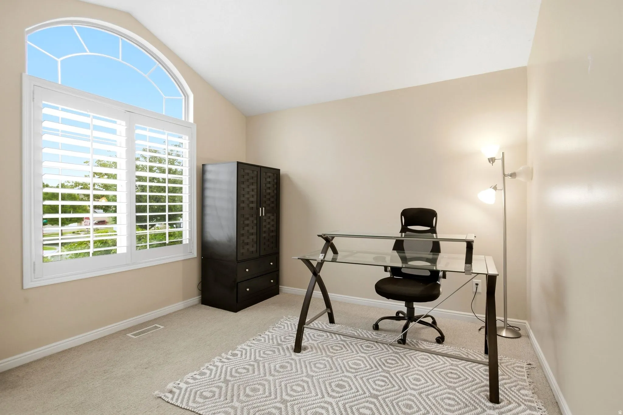 Arched window with plantation shutters, vaulted ceiling, and neutral carpet flooring