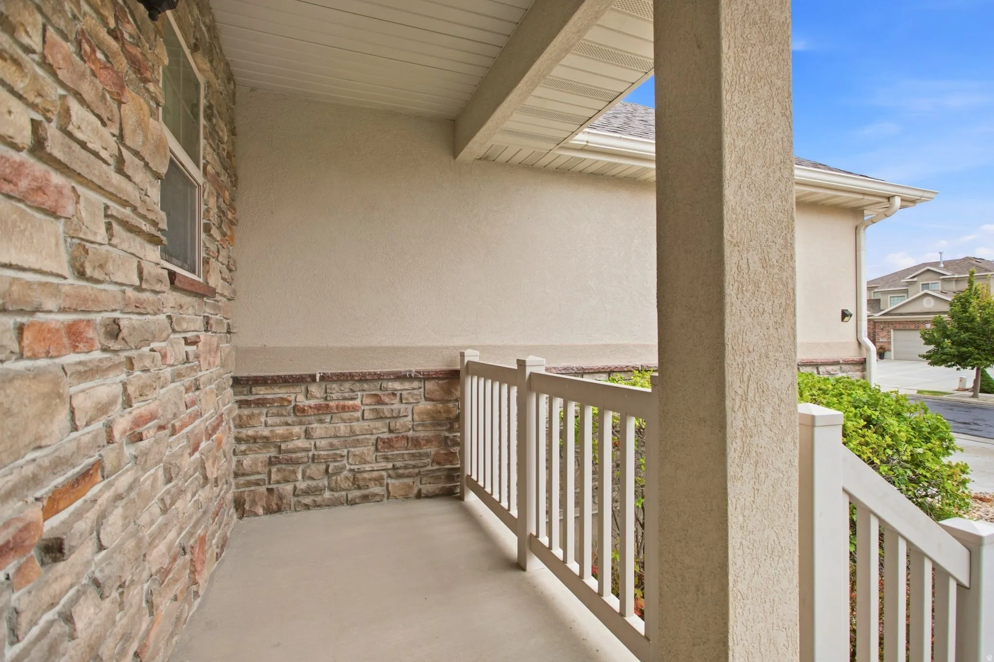 Covered porch with horizontal white railings, concrete flooring, and mixed-material exterior featuring exposed brick and stucco walls